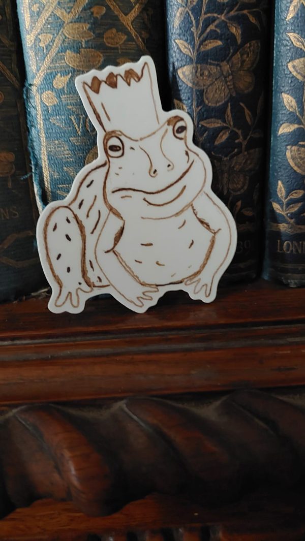 Frog with crown sticker in front of blue books